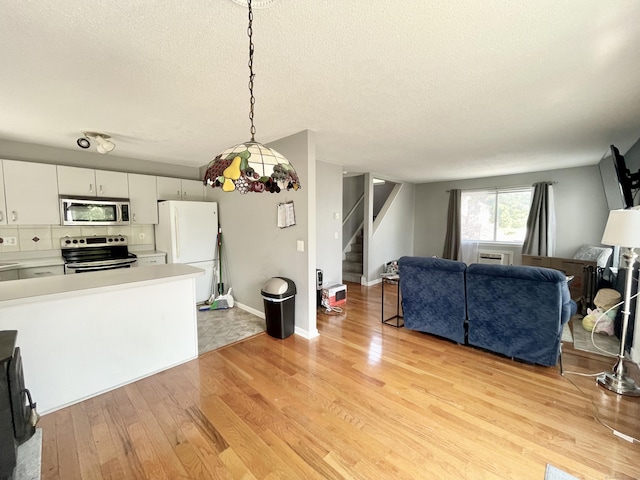 kitchen featuring appliances with stainless steel finishes, white cabinets, hanging light fixtures, a textured ceiling, and light hardwood / wood-style flooring