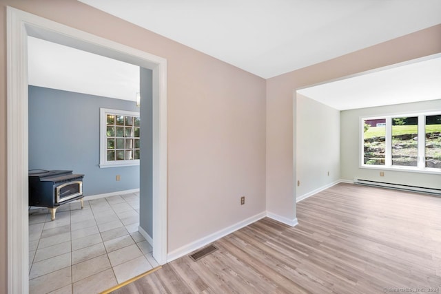 unfurnished room with light hardwood / wood-style flooring, a baseboard radiator, plenty of natural light, and a wood stove