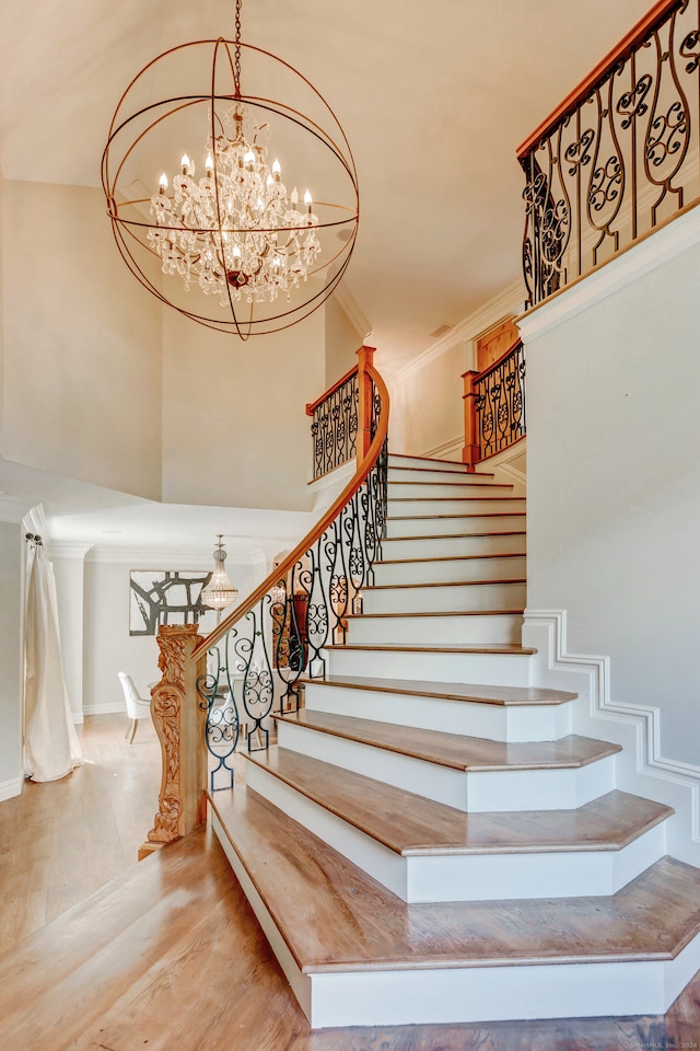 stairway featuring crown molding, hardwood / wood-style flooring, a towering ceiling, and a chandelier