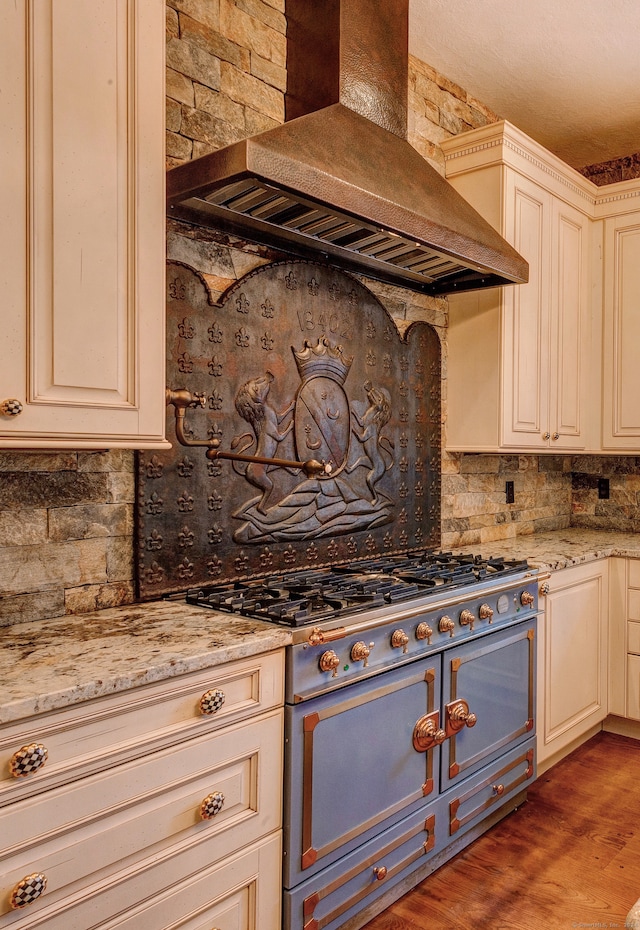 kitchen with light stone countertops, backsplash, light hardwood / wood-style floors, stainless steel range, and custom range hood