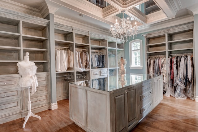 walk in closet with beam ceiling, a chandelier, coffered ceiling, and light wood-type flooring