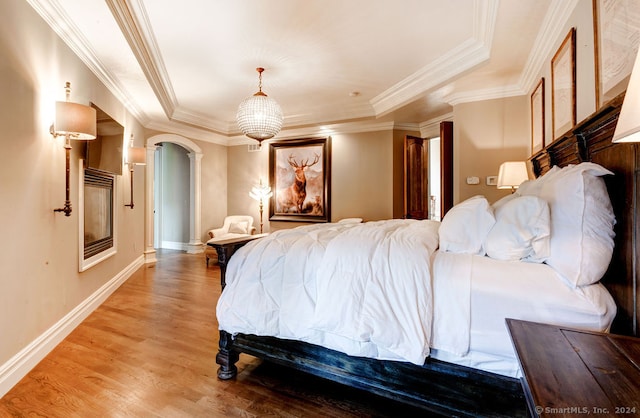 bedroom with light hardwood / wood-style floors, crown molding, a chandelier, and a tray ceiling