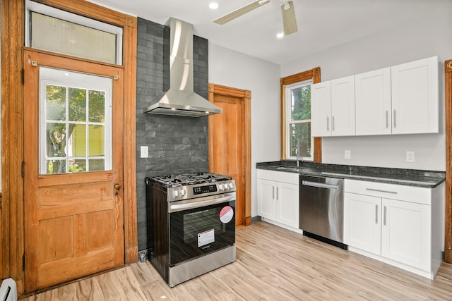 kitchen featuring light wood-type flooring, white cabinetry, stainless steel appliances, wall chimney exhaust hood, and a wealth of natural light