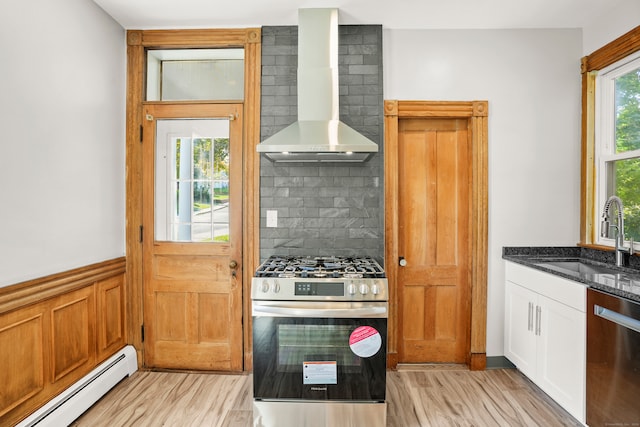 kitchen with wall chimney range hood, a baseboard heating unit, dark stone counters, sink, and appliances with stainless steel finishes