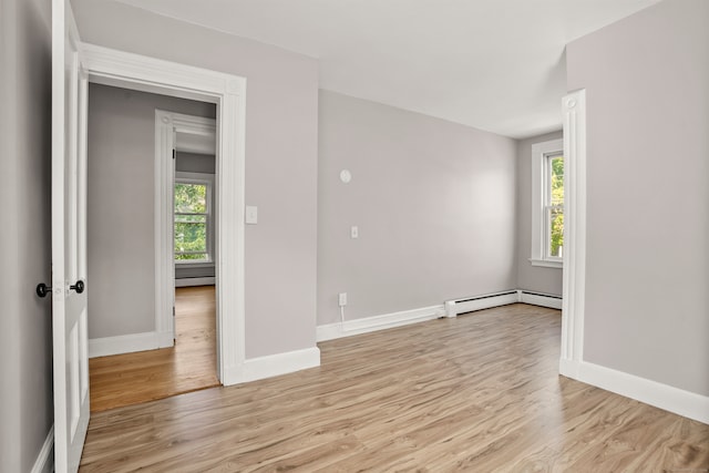 empty room featuring baseboard heating, a wealth of natural light, and light wood-type flooring