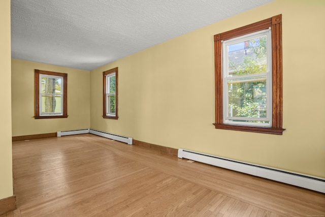 empty room featuring light wood-type flooring, a healthy amount of sunlight, a textured ceiling, and baseboard heating