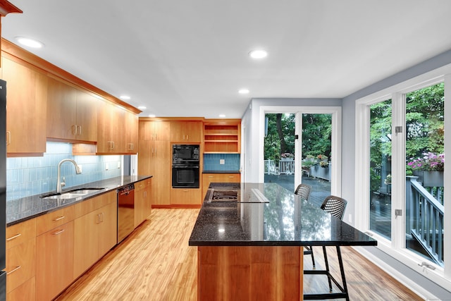 kitchen featuring light wood-type flooring, decorative backsplash, dark stone counters, and black microwave