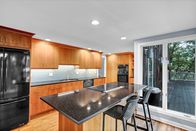 kitchen with black appliances, light wood-type flooring, sink, and a center island