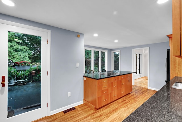 kitchen with black appliances, light hardwood / wood-style floors, and dark stone counters