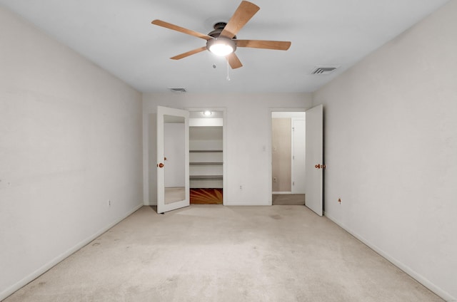 unfurnished bedroom with light carpet, a spacious closet, and ceiling fan