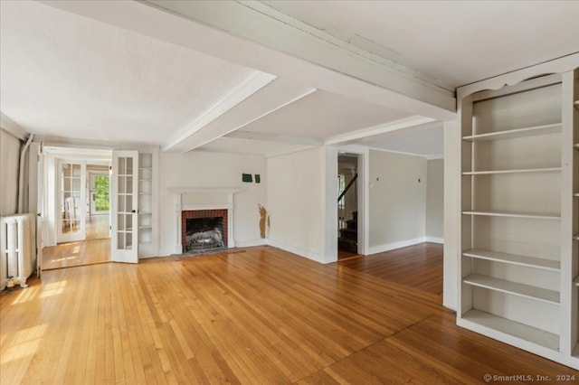 unfurnished living room featuring ornamental molding, hardwood / wood-style floors, a fireplace, and french doors