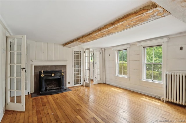 unfurnished living room featuring french doors, beamed ceiling, radiator, and light wood-type flooring