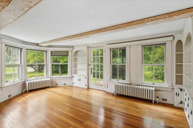 unfurnished sunroom with beamed ceiling, radiator heating unit, and a healthy amount of sunlight