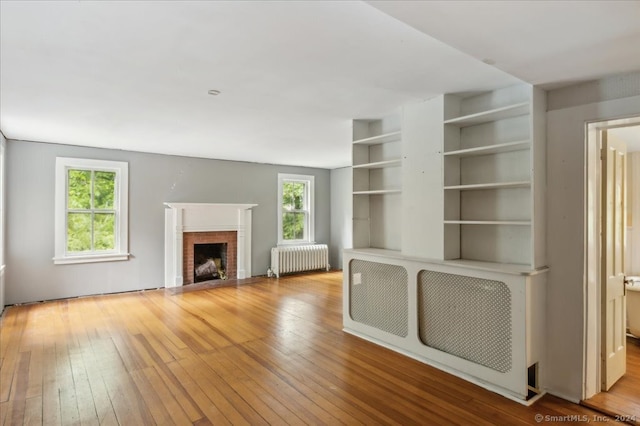 unfurnished living room with light hardwood / wood-style floors, radiator heating unit, a fireplace, and built in shelves