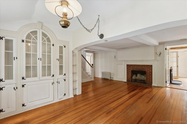 unfurnished living room featuring lofted ceiling, a fireplace, wood-type flooring, and radiator