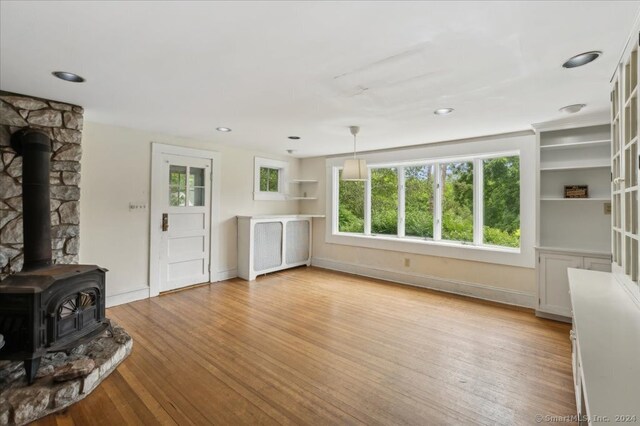 unfurnished living room featuring light hardwood / wood-style floors, a wood stove, and built in shelves