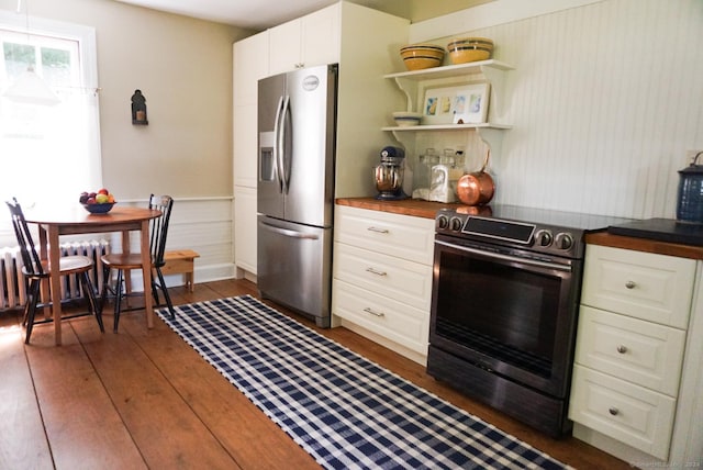 kitchen featuring appliances with stainless steel finishes, white cabinetry, butcher block counters, radiator heating unit, and dark hardwood / wood-style flooring