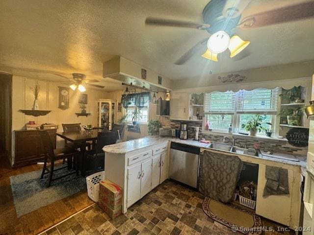 kitchen featuring stainless steel dishwasher, a peninsula, white cabinets, and light countertops