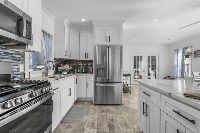 kitchen featuring white cabinets, light hardwood / wood-style floors, stainless steel appliances, light stone countertops, and french doors