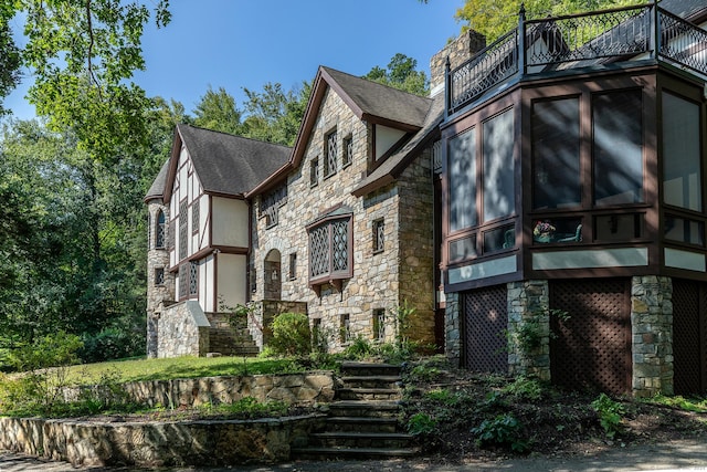 view of side of home featuring stone siding, a balcony, a chimney, and a sunroom