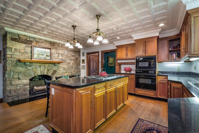 kitchen featuring pendant lighting, hardwood / wood-style floors, a fireplace, black appliances, and a kitchen island