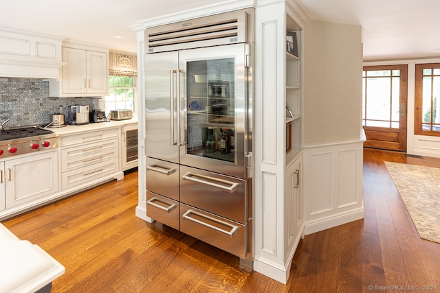 kitchen with hardwood / wood-style floors, tasteful backsplash, premium range hood, stainless steel appliances, and white cabinets