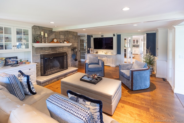 living room featuring light wood-type flooring, french doors, beamed ceiling, and a stone fireplace