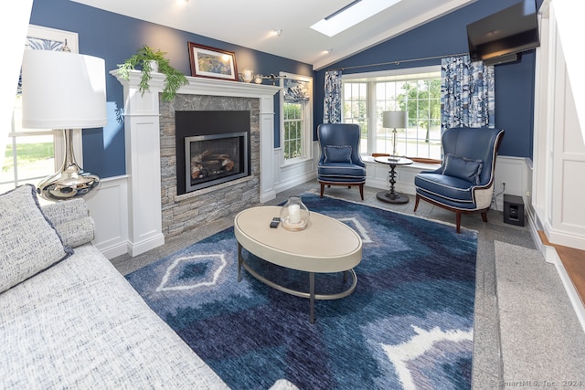 living room with hardwood / wood-style floors, a stone fireplace, and lofted ceiling with skylight