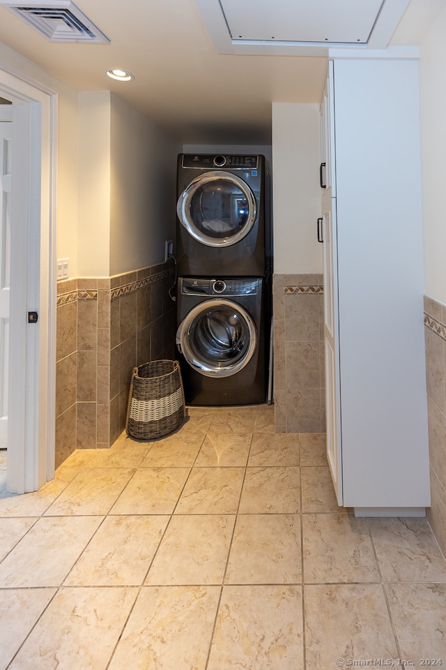 clothes washing area featuring tile walls, stacked washing maching and dryer, and light tile patterned floors