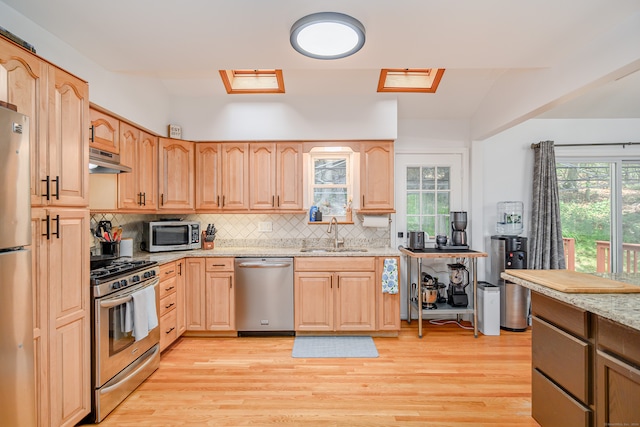 kitchen featuring light stone countertops, light hardwood / wood-style flooring, stainless steel appliances, and tasteful backsplash