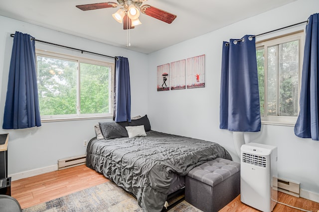 bedroom with wood-type flooring, multiple windows, a baseboard radiator, and ceiling fan