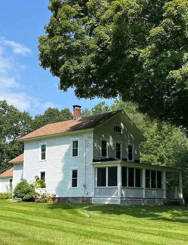 back of property featuring a sunroom and a lawn