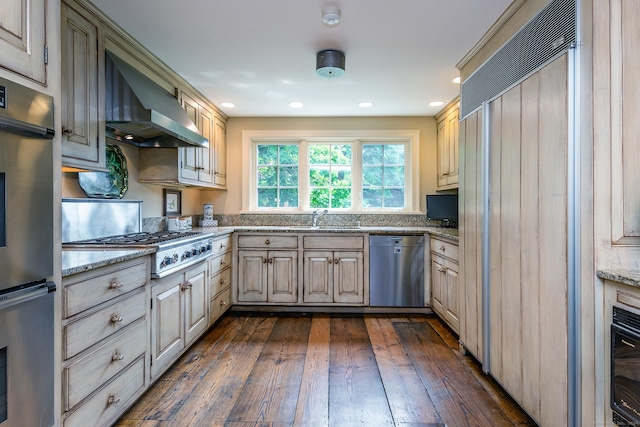 kitchen featuring dark wood-type flooring, sink, stainless steel appliances, light stone countertops, and wall chimney range hood