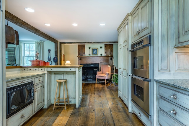 kitchen featuring light stone counters, double oven, cream cabinets, and black microwave