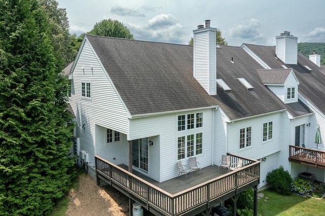 rear view of property featuring a deck, a shingled roof, and a chimney