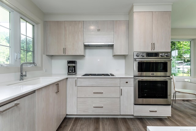 kitchen with dark wood-type flooring, light brown cabinetry, black cooktop, stainless steel double oven, and a sink