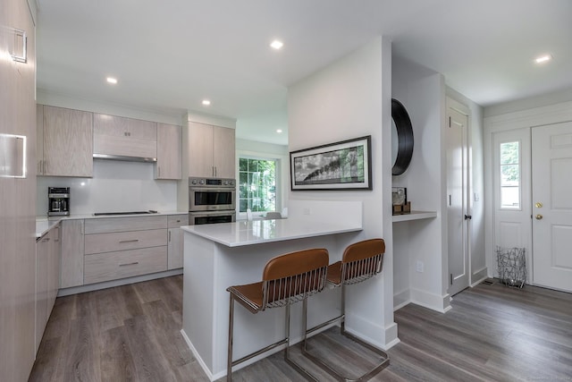 kitchen featuring wood finished floors, stovetop, light countertops, a kitchen breakfast bar, and modern cabinets