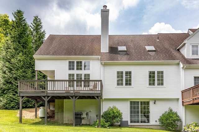 back of house featuring a deck, a chimney, a yard, and a shingled roof