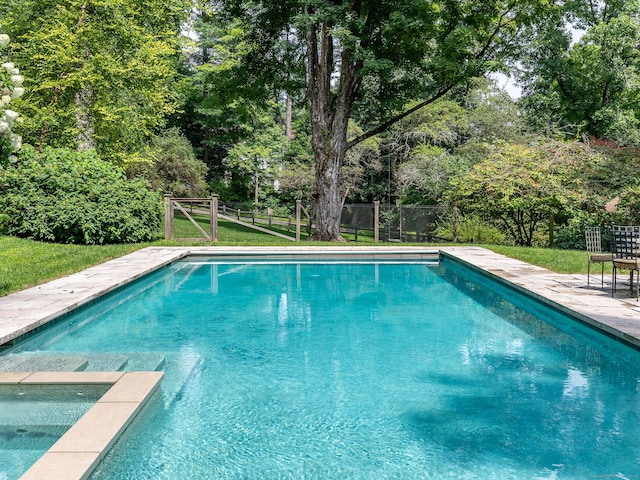 view of pool featuring a pool with connected hot tub, fence, and a lawn