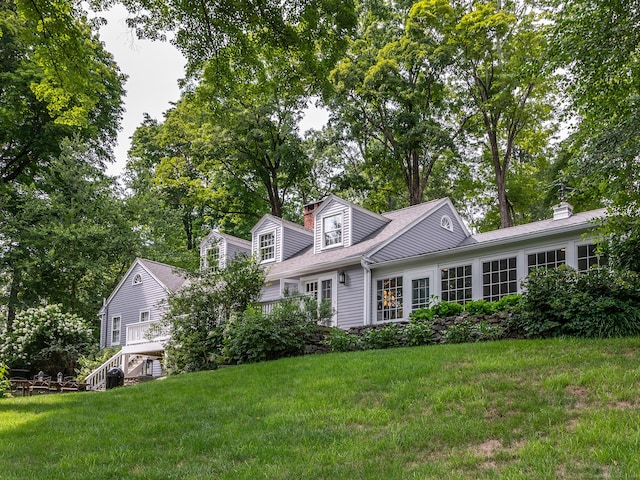 cape cod house with a chimney, stairway, and a front yard