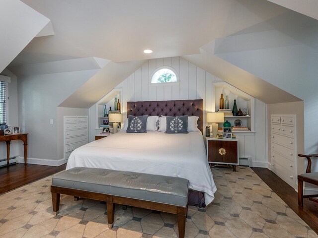 bedroom with a baseboard heating unit, vaulted ceiling, wood finished floors, and baseboards