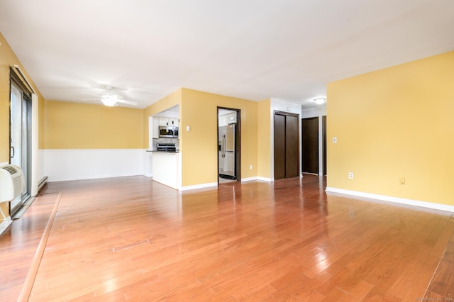 spare room featuring ceiling fan, light wood finished floors, a wall mounted AC, and baseboards