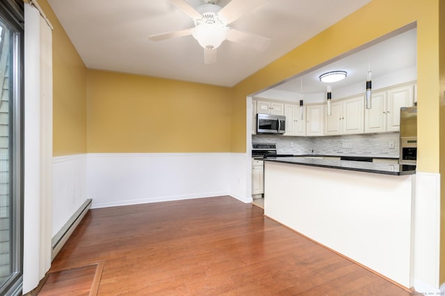 kitchen with wainscoting, dark countertops, a baseboard radiator, appliances with stainless steel finishes, and wood finished floors