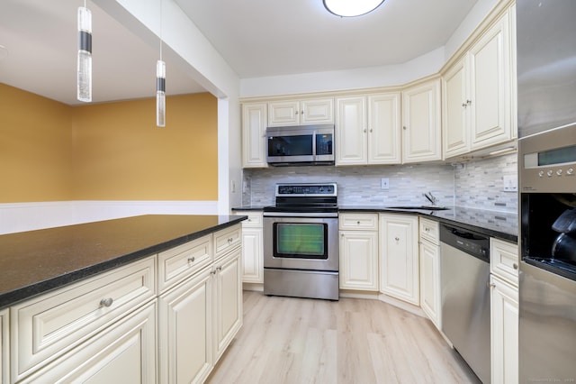 kitchen with a sink, appliances with stainless steel finishes, light wood-type flooring, backsplash, and dark countertops