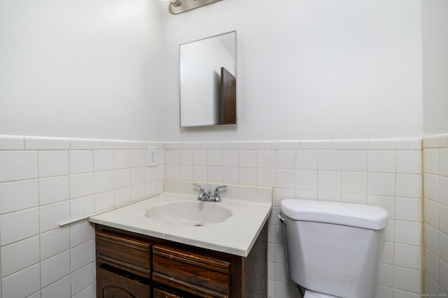 half bath with toilet, wainscoting, tile walls, and vanity