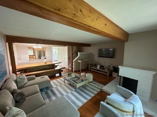 living room with beamed ceiling, a textured ceiling, a brick fireplace, a notable chandelier, and hardwood / wood-style flooring