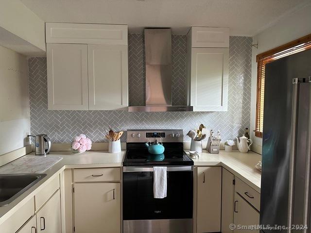 kitchen featuring wall chimney range hood, backsplash, stainless steel appliances, and white cabinets