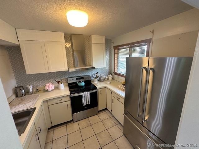 kitchen featuring wall chimney exhaust hood, stainless steel appliances, sink, and white cabinets