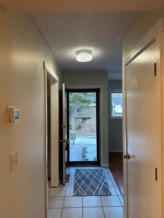 doorway with a wealth of natural light, light tile patterned floors, and a textured ceiling