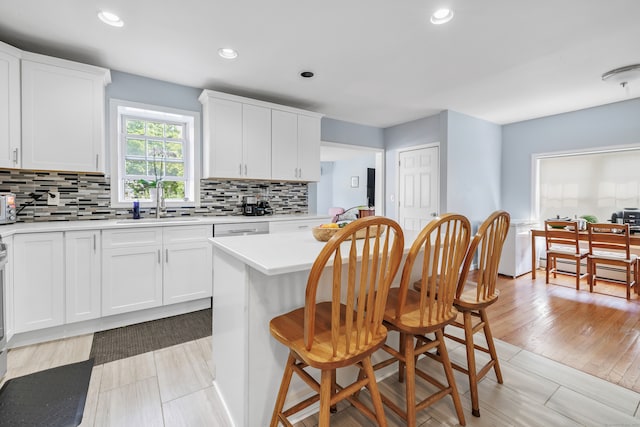 kitchen with white cabinets, decorative backsplash, sink, dishwasher, and light hardwood / wood-style flooring